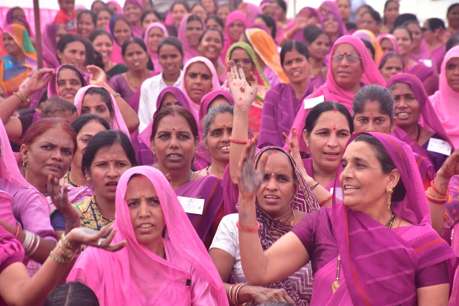 Women from a village collective gathered together, many raising their hands